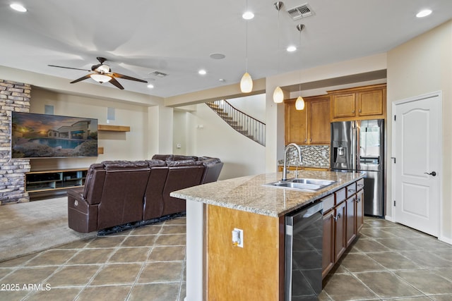 kitchen featuring sink, light stone counters, hanging light fixtures, appliances with stainless steel finishes, and an island with sink