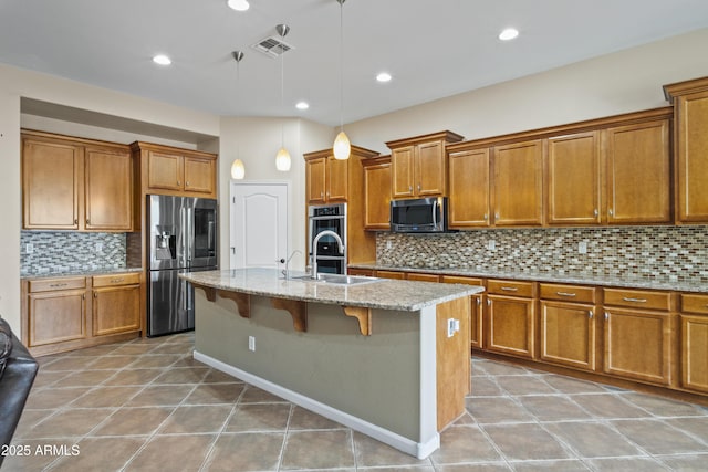 kitchen featuring an island with sink, sink, a kitchen breakfast bar, light stone counters, and stainless steel appliances