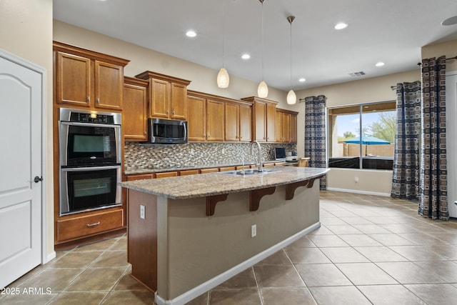 kitchen with sink, a breakfast bar area, stainless steel appliances, light stone counters, and an island with sink