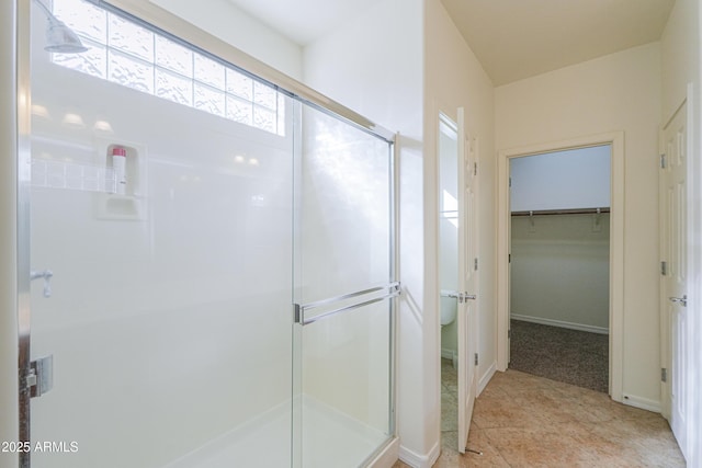 bathroom with a stall shower, baseboards, and a walk in closet