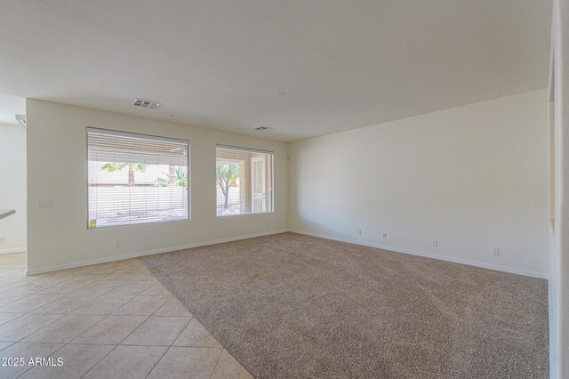 empty room featuring light tile patterned floors, light carpet, visible vents, and baseboards