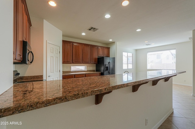 kitchen with visible vents, black appliances, dark stone countertops, a peninsula, and a kitchen bar