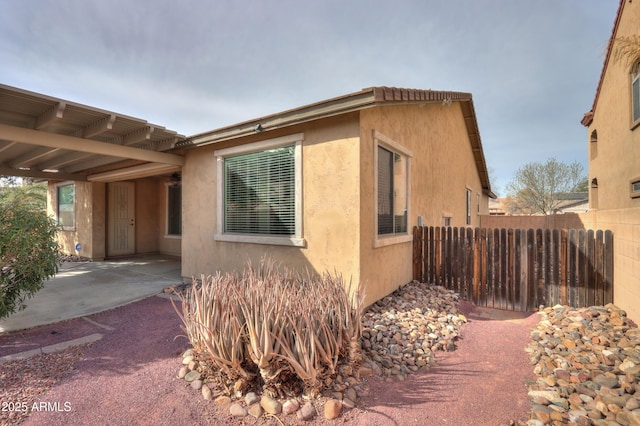 view of side of home featuring a patio, fence, and stucco siding