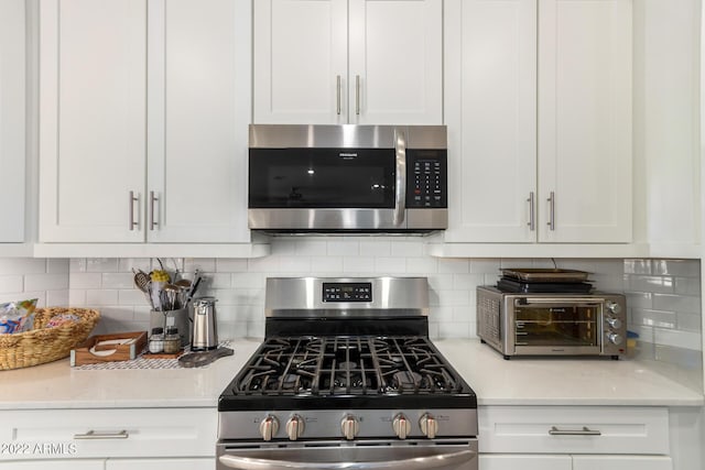 kitchen with white cabinets, decorative backsplash, light stone counters, and appliances with stainless steel finishes