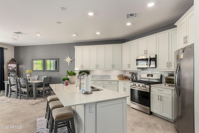 kitchen with tasteful backsplash, stainless steel appliances, sink, white cabinets, and an island with sink