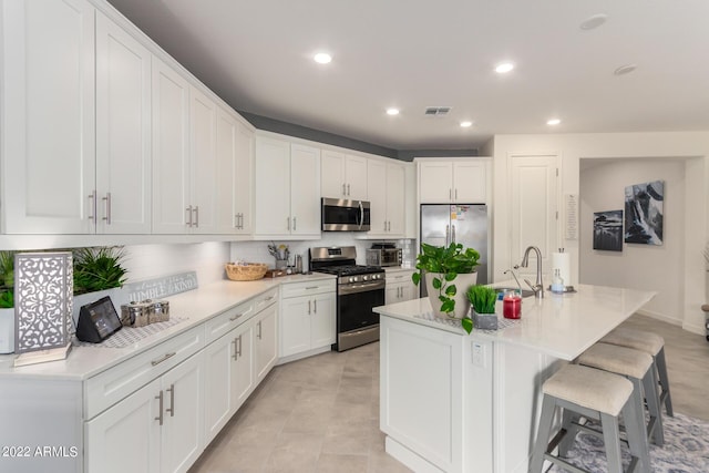 kitchen with white cabinets, decorative backsplash, an island with sink, appliances with stainless steel finishes, and a kitchen bar