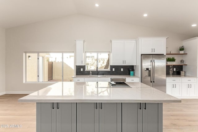 kitchen with white cabinets, a spacious island, stainless steel refrigerator with ice dispenser, open shelves, and a sink