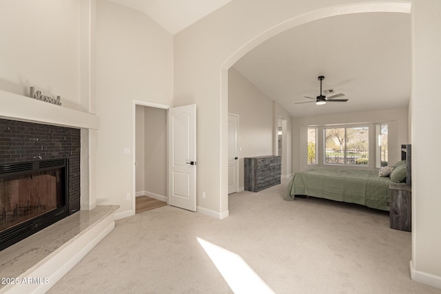 carpeted bedroom featuring lofted ceiling, a fireplace with raised hearth, a ceiling fan, and baseboards