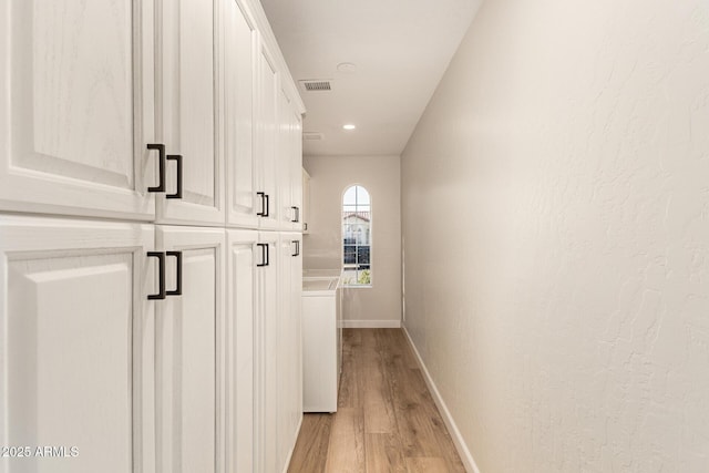 hall with light wood-type flooring, visible vents, baseboards, and a textured wall