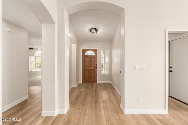 entrance foyer with light wood-style flooring, arched walkways, and baseboards