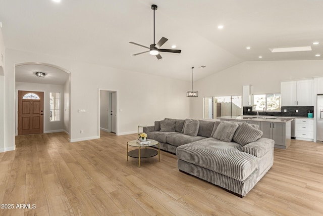 living area with baseboards, arched walkways, ceiling fan, light wood-style floors, and high vaulted ceiling