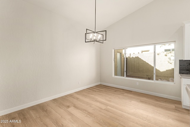 spare room with vaulted ceiling, light wood-type flooring, baseboards, and an inviting chandelier