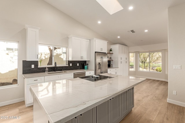 kitchen with a skylight, stainless steel appliances, decorative backsplash, white cabinetry, and a sink