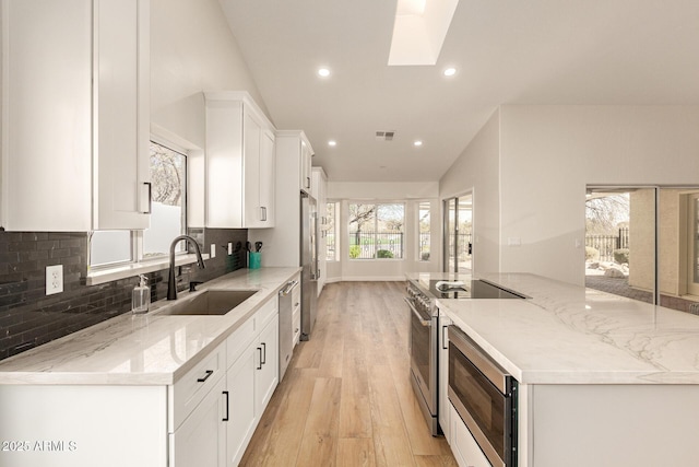 kitchen with tasteful backsplash, a spacious island, appliances with stainless steel finishes, white cabinetry, and a sink