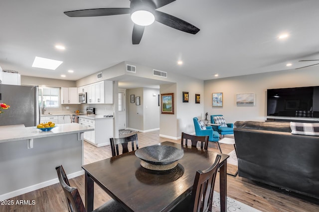 dining room with ceiling fan, light hardwood / wood-style floors, sink, and a skylight