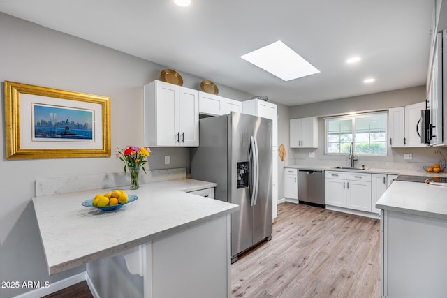 kitchen with kitchen peninsula, white cabinets, a skylight, and stainless steel appliances