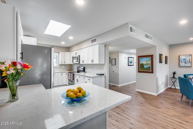 kitchen featuring white cabinets, a skylight, stainless steel appliances, kitchen peninsula, and light wood-type flooring