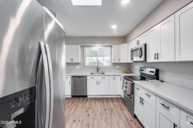 kitchen featuring white cabinetry, stainless steel appliances, light hardwood / wood-style floors, sink, and light stone counters