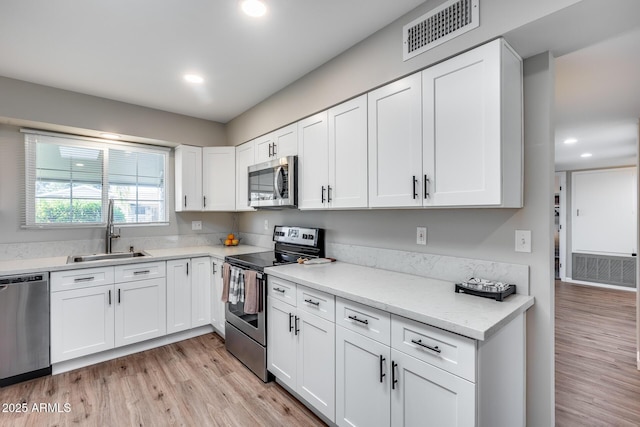 kitchen with light stone countertops, sink, white cabinets, light hardwood / wood-style flooring, and stainless steel appliances