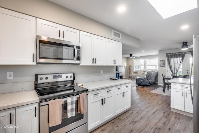 kitchen with ceiling fan, appliances with stainless steel finishes, light wood-type flooring, white cabinetry, and light stone counters