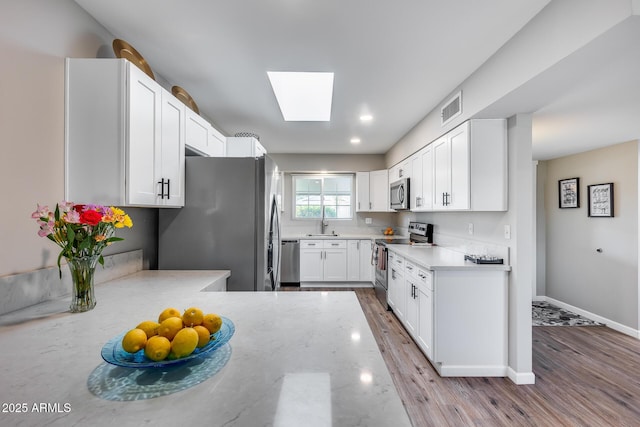 kitchen with sink, white cabinets, a skylight, light hardwood / wood-style floors, and stainless steel appliances