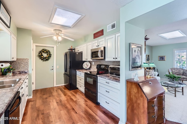 kitchen with a skylight, sink, white cabinets, hardwood / wood-style flooring, and black appliances