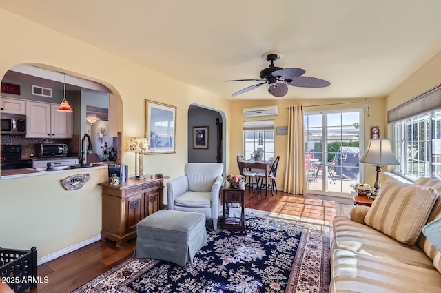 living room with hardwood / wood-style flooring, ceiling fan, sink, and a wall unit AC