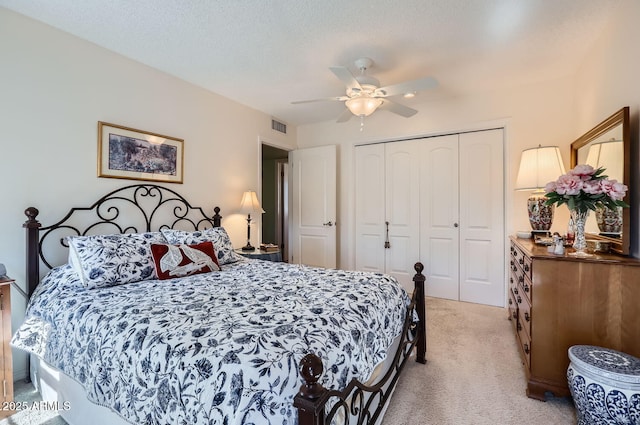 bedroom with ceiling fan, light carpet, a textured ceiling, and a closet