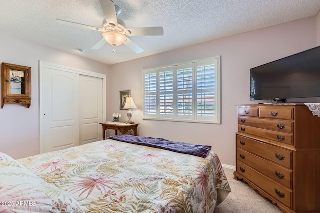 bedroom featuring ceiling fan, light colored carpet, a closet, and a textured ceiling