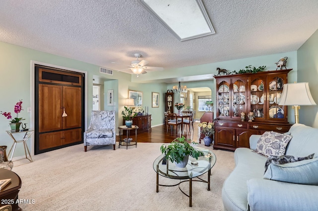 carpeted living room featuring ceiling fan with notable chandelier, a textured ceiling, and a skylight