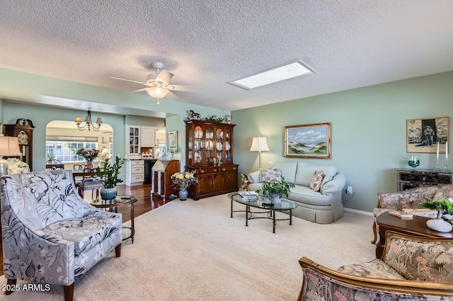 carpeted living room with a skylight, ceiling fan with notable chandelier, and a textured ceiling