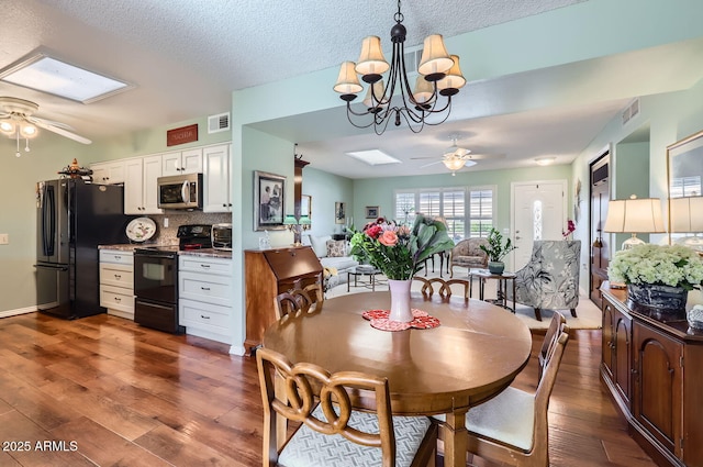 dining area featuring dark hardwood / wood-style floors, a skylight, ceiling fan with notable chandelier, and a textured ceiling