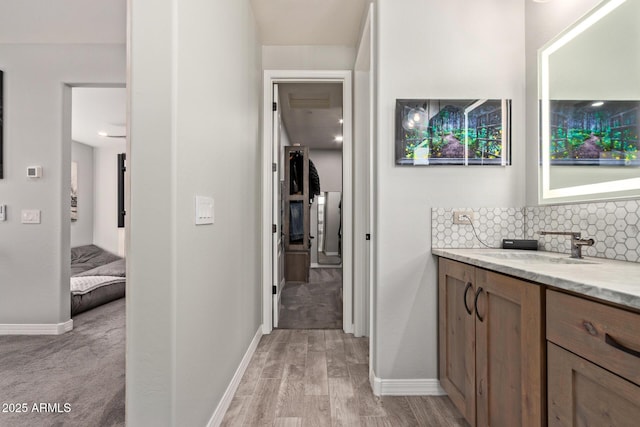 bathroom with baseboards, wood finished floors, vanity, and decorative backsplash