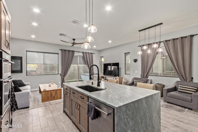 kitchen featuring visible vents, dishwasher, open floor plan, light wood-style floors, and a sink