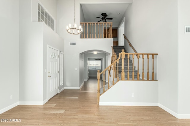 entrance foyer with ceiling fan with notable chandelier, light hardwood / wood-style flooring, and a towering ceiling