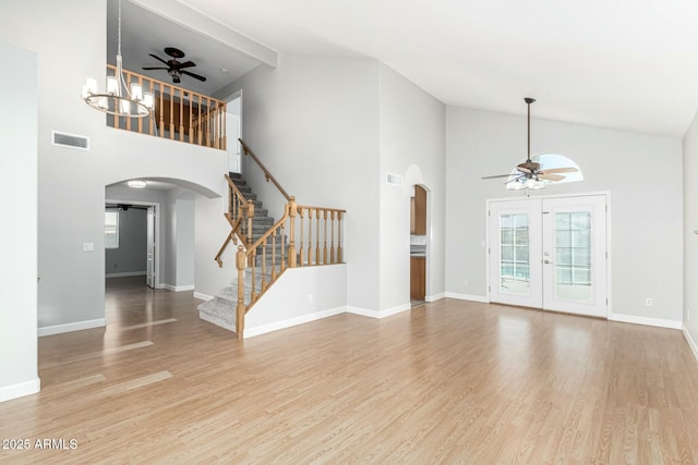 unfurnished living room featuring ceiling fan with notable chandelier, high vaulted ceiling, french doors, and light wood-type flooring