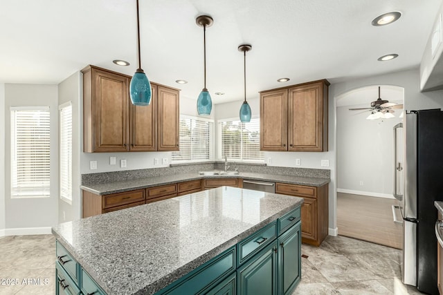 kitchen with sink, hanging light fixtures, appliances with stainless steel finishes, a kitchen island, and ceiling fan