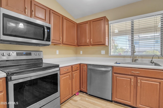 kitchen with stainless steel appliances, a sink, vaulted ceiling, light countertops, and light wood finished floors