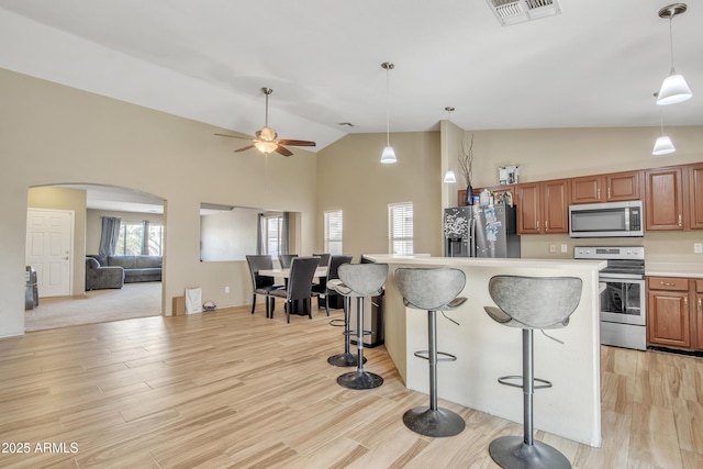 kitchen featuring arched walkways, stainless steel appliances, visible vents, light wood-style floors, and a kitchen breakfast bar