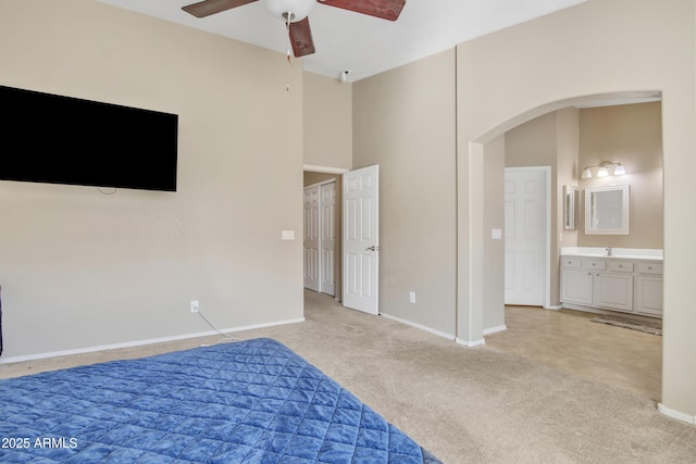 unfurnished bedroom featuring arched walkways, a high ceiling, light carpet, connected bathroom, and baseboards