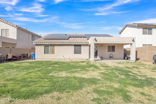 rear view of property with a patio, a fenced backyard, a lawn, roof mounted solar panels, and stucco siding