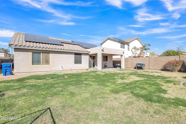 back of house with a lawn, roof mounted solar panels, a tile roof, and stucco siding