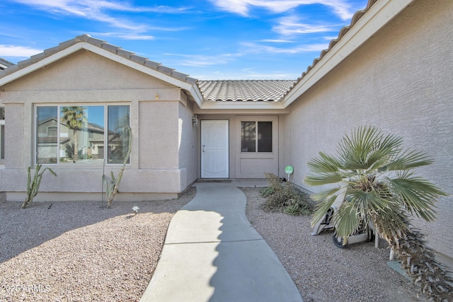 view of exterior entry with a tile roof and stucco siding