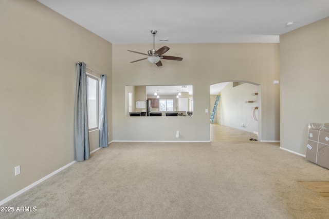 unfurnished living room featuring arched walkways, carpet, a wealth of natural light, and a ceiling fan