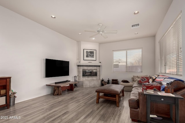 living room featuring ceiling fan, a tiled fireplace, and light hardwood / wood-style flooring