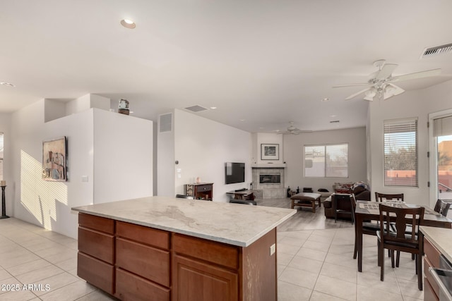 kitchen featuring ceiling fan, a fireplace, a center island, light stone countertops, and light tile patterned floors