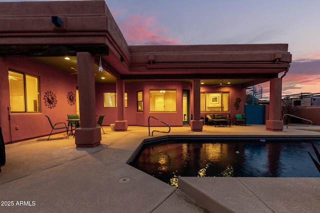 pool at dusk with ceiling fan and a patio area