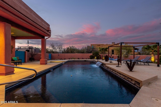 pool at dusk with pool water feature, a pergola, and a patio