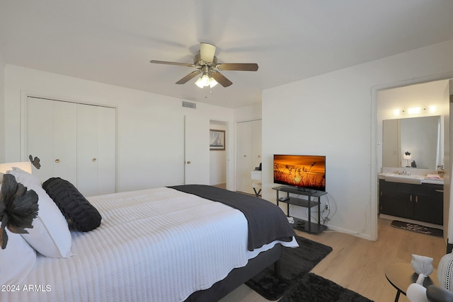 bedroom with light hardwood / wood-style flooring, ensuite bath, ceiling fan, and multiple closets