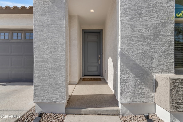 view of exterior entry with stucco siding and a garage